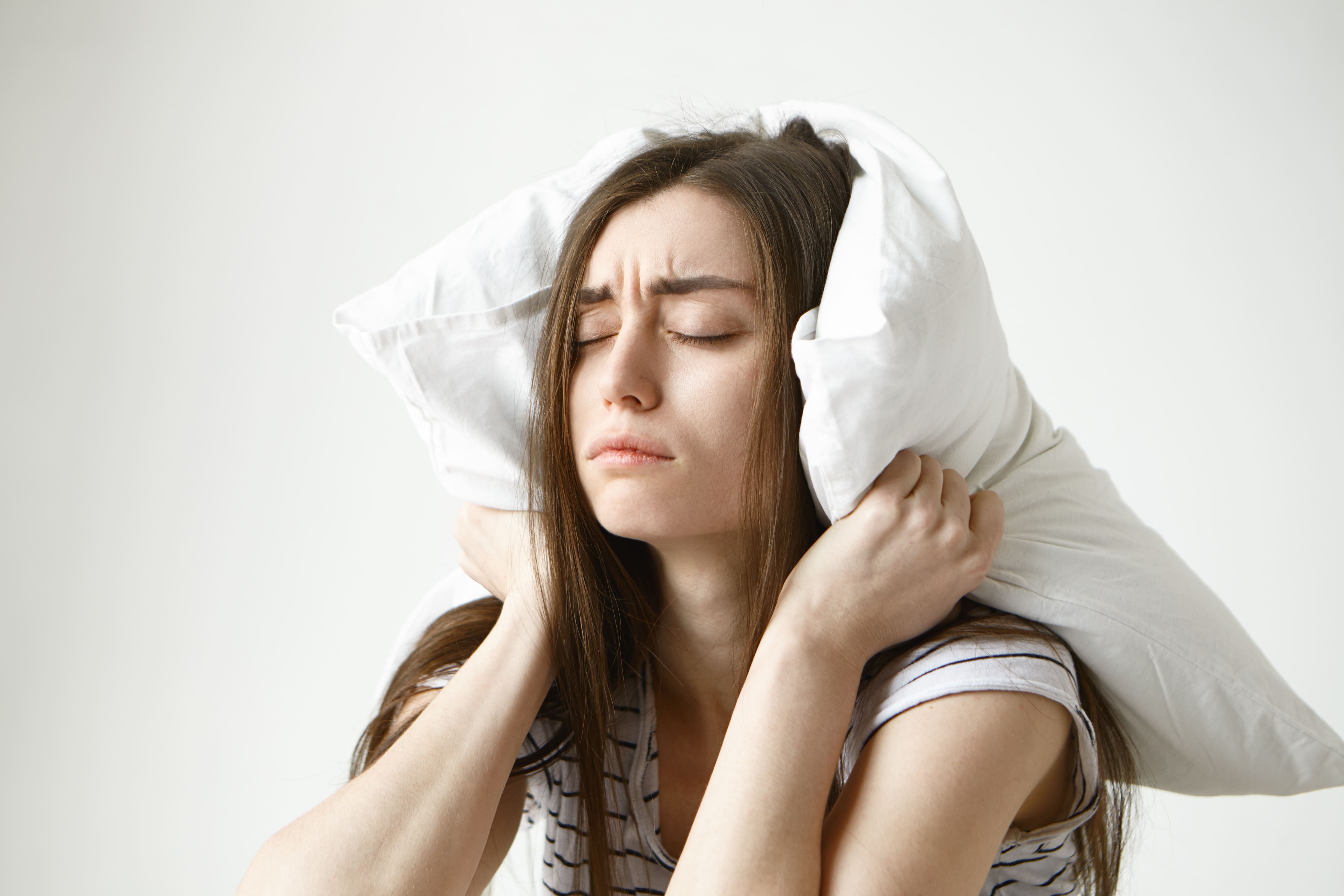 pretty-student-woman-in-striped-t-shirt-trying-to-have-some-sleep-sitting-in-bedroom-with-pillow-on-her-head-closing-eyes (1)